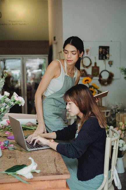A florist from South Kensington Flowers arranged a bouquet of fresh, vibrant flowers, including pink and white roses, lavender, and green foliage, on a rustic wooden table inside a well-lit shop. The